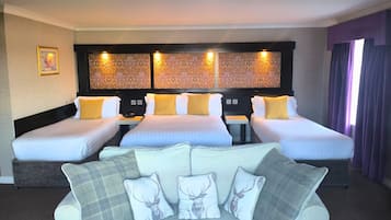 A hotel room with three single beds, a sofa with patterned cushions, and a decorative headboard.
