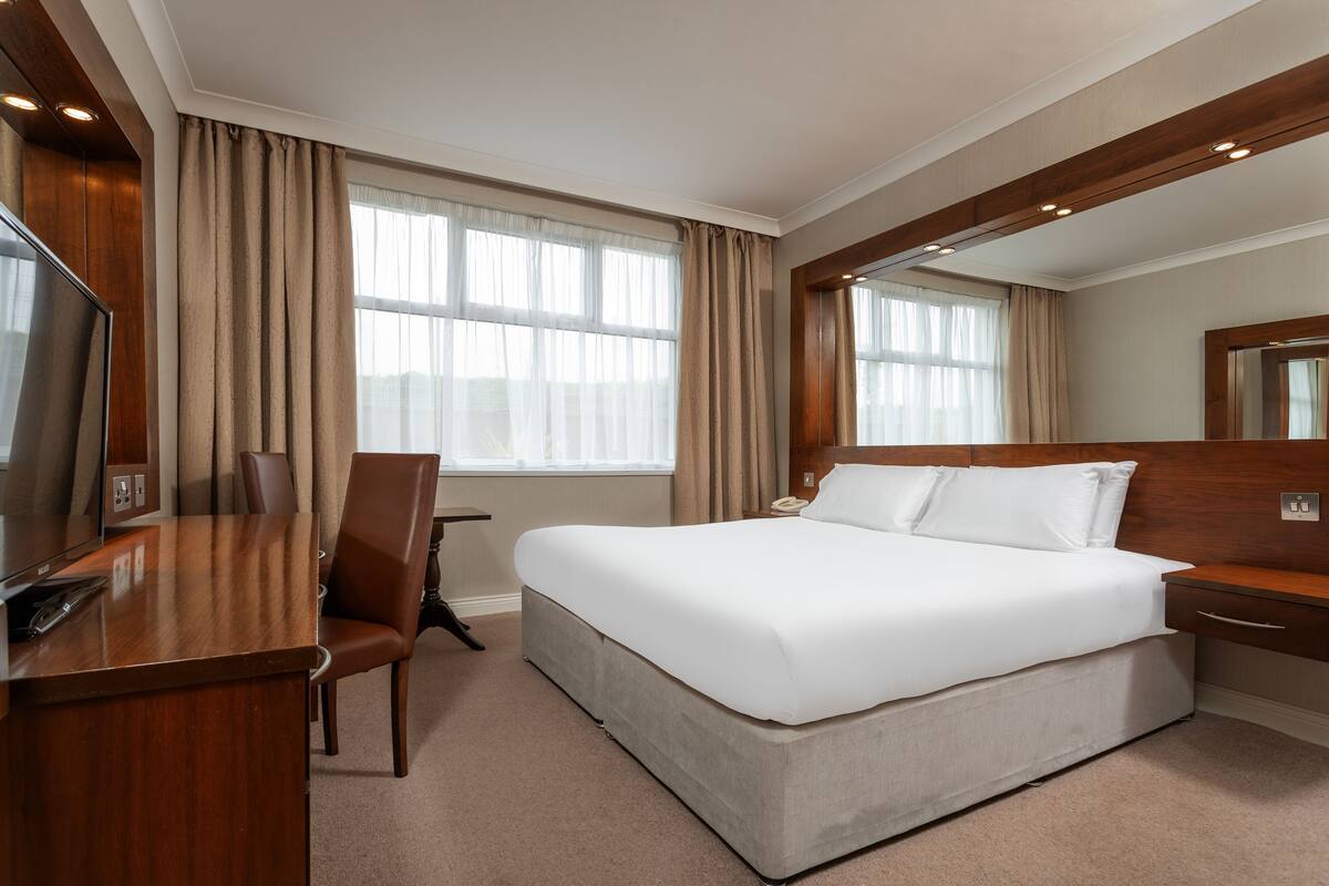 A hotel room with a large bed, a desk with a chair, a television, and a large mirror.