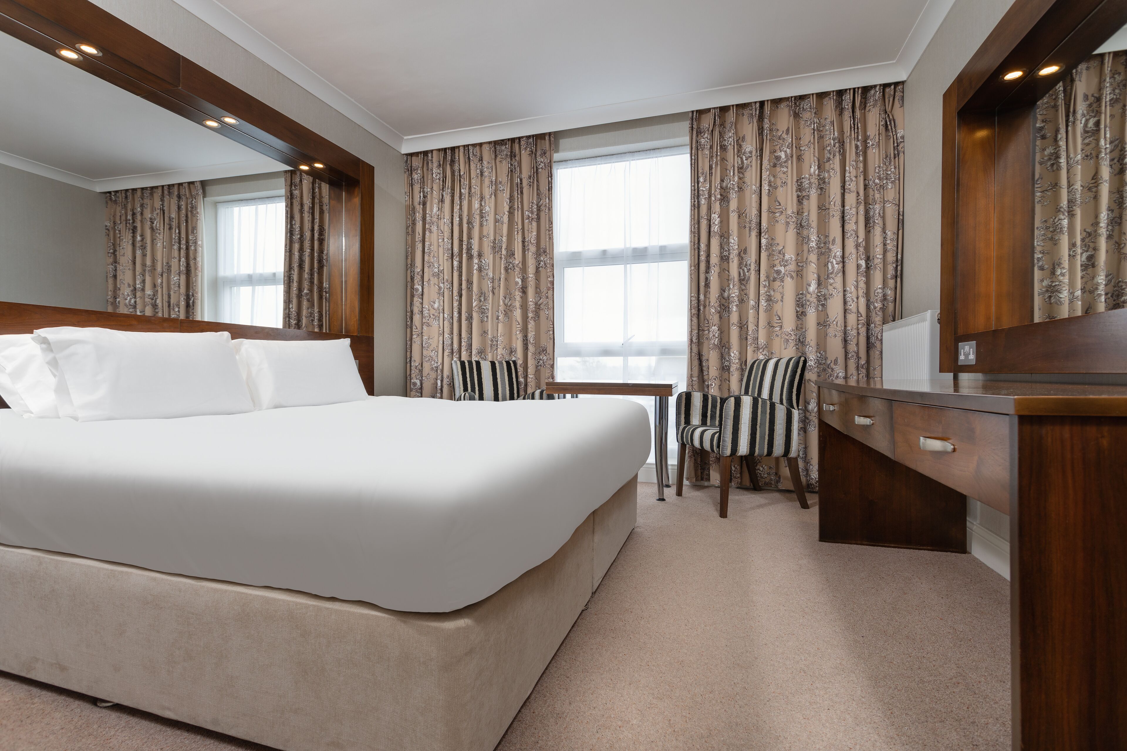 A hotel room with a large bed, a desk, a chair, and curtains.