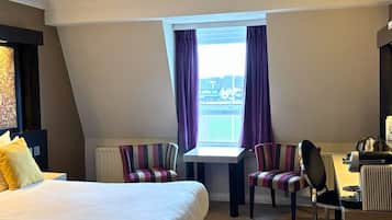 A hotel room with a large bed, a desk, two chairs, and a window with curtains.