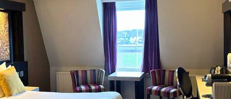 Une chambre d’hôtel avec un grand lit, un bureau, deux chaises et une fenêtre avec des rideaux.