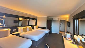 A hotel room with three beds, a desk with a coffee machine, and a large mirror.