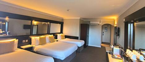 A hotel room with three beds, a desk with a coffee machine, and a large mirror.