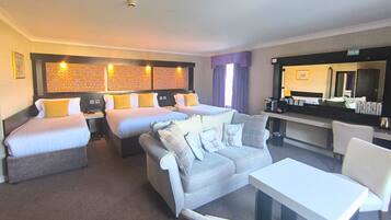 A hotel room with two beds, a sofa, a table, a desk, and a bathroom.
