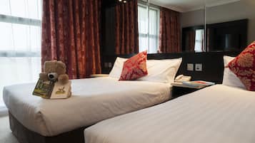 Ein Hotelzimmer mit zwei Betten, einem großen Spiegel, einem Teddybären und einem Buch auf dem Bett links.