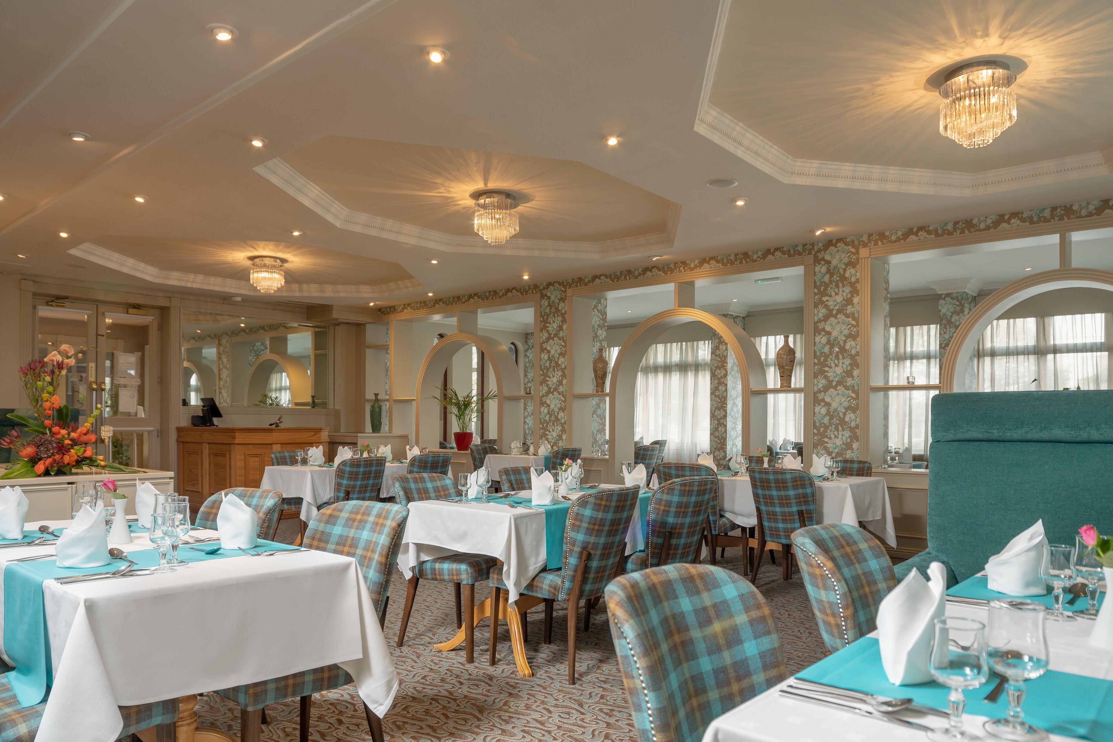 A dining area with round tables, teal and plaid chairs, and chandeliers.