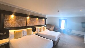 Habitación de hotel con dos camas, cabecera con paneles decorativos, una mesita y una silla.