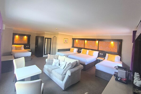 Habitación de hotel con dos camas individuales, un sofá, una mesita y una silla.