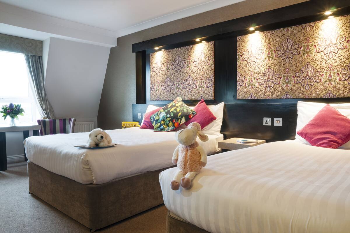 A hotel room with two beds, a large decorative headboard, and a window with curtains.