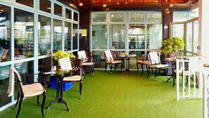 Un espacio interior con asientos, mesas, ventanas amplias y suelo de césped artificial.