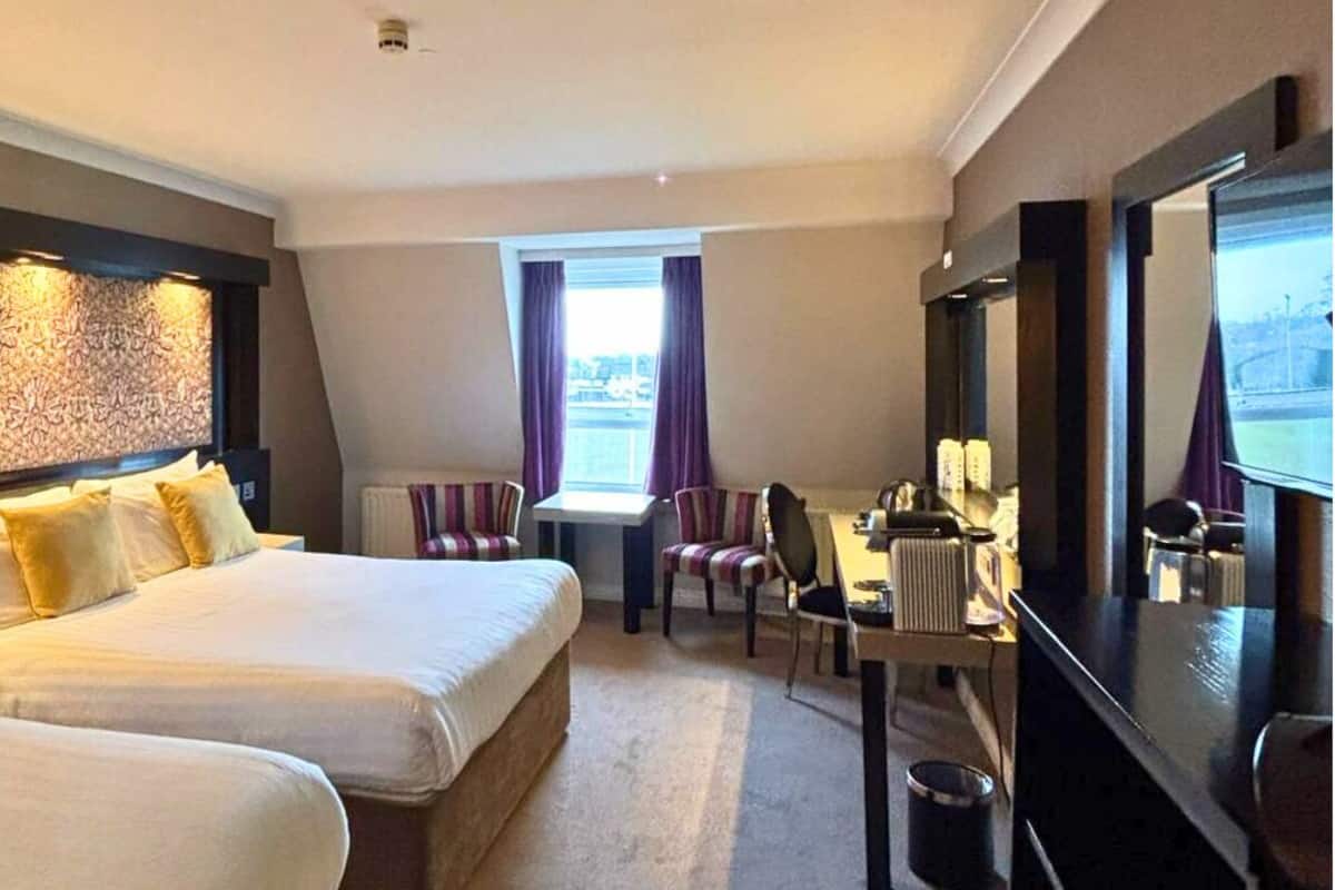 A hotel room with two beds, a desk, a chair, and a television.