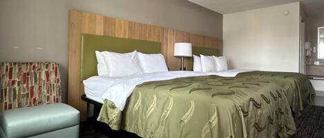 A hotel room with a bed, a small seating area, a lamp, and a mirror.