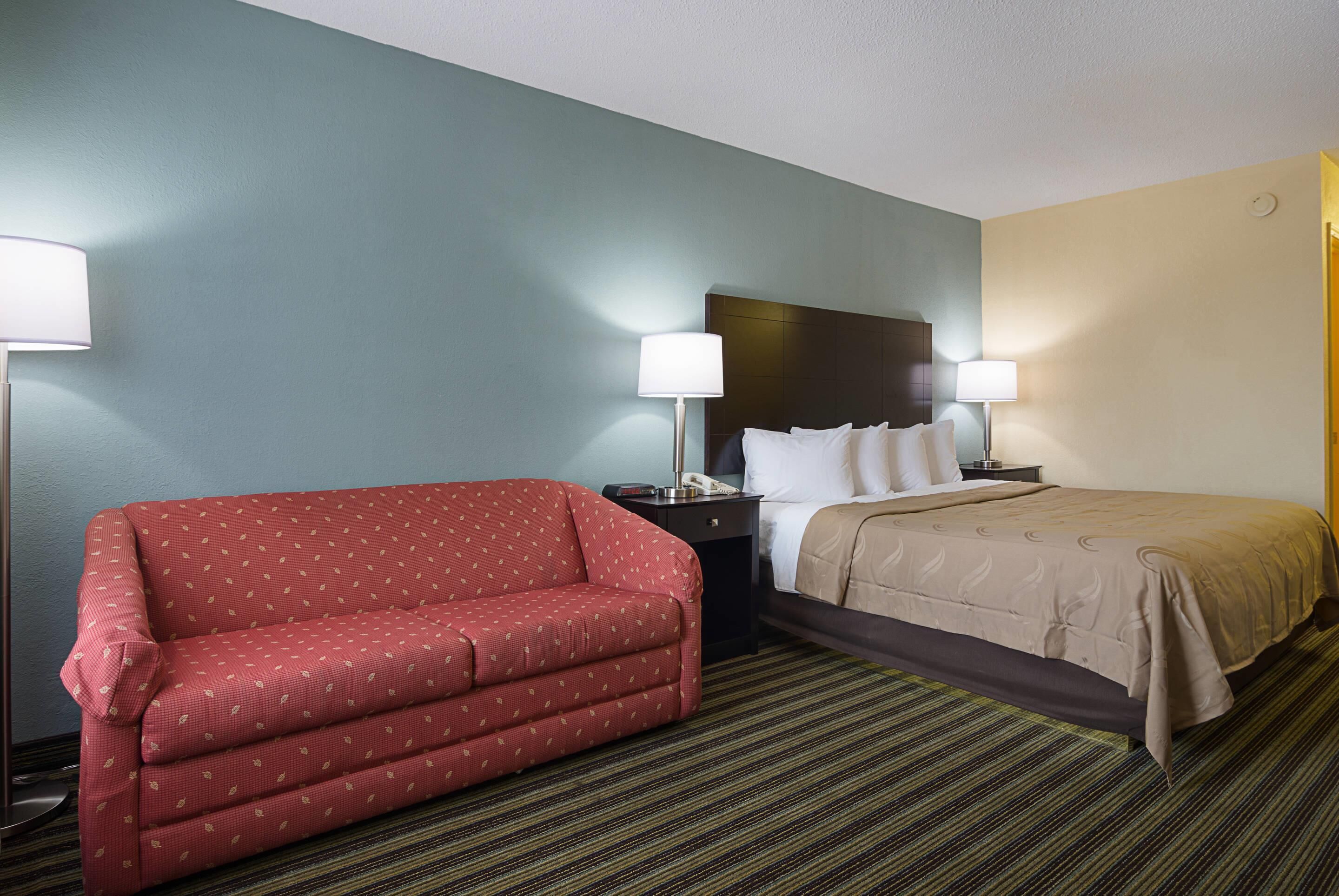 A hotel room with a red sofa, a bed with a beige bedspread, and two bedside lamps.