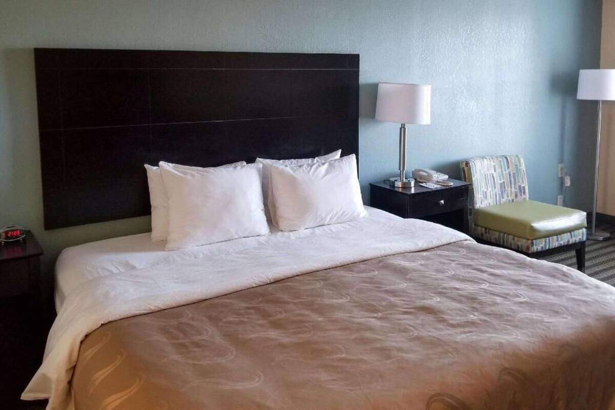 Una habitación de hotel con una cama grande, una mesita de noche con lámpara, una silla y un teléfono.
