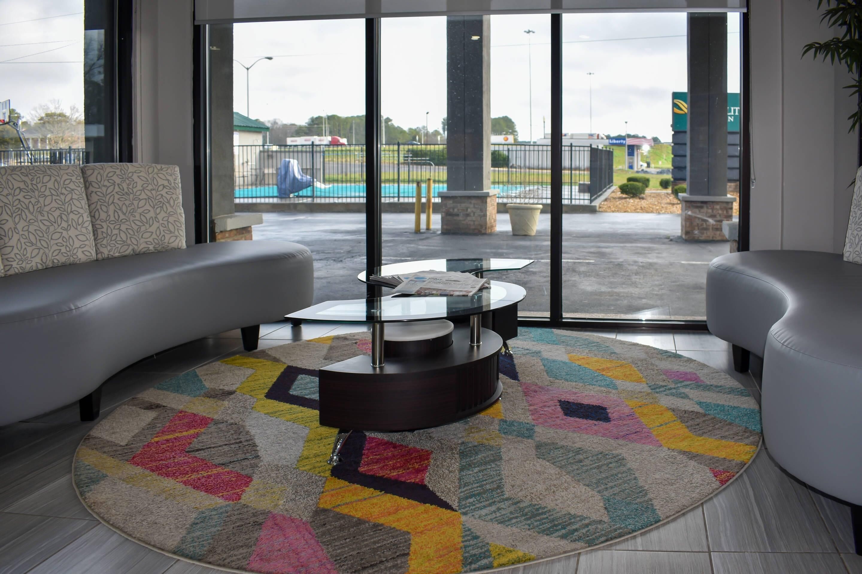 A modern hotel lobby with a large window, a round coffee table, and a colorful rug.