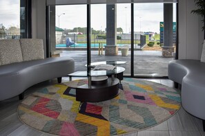 A modern hotel lobby with a large window, a round coffee table, and a colorful rug. - Quality Inn Calhoun North I-75 (Calhoun)