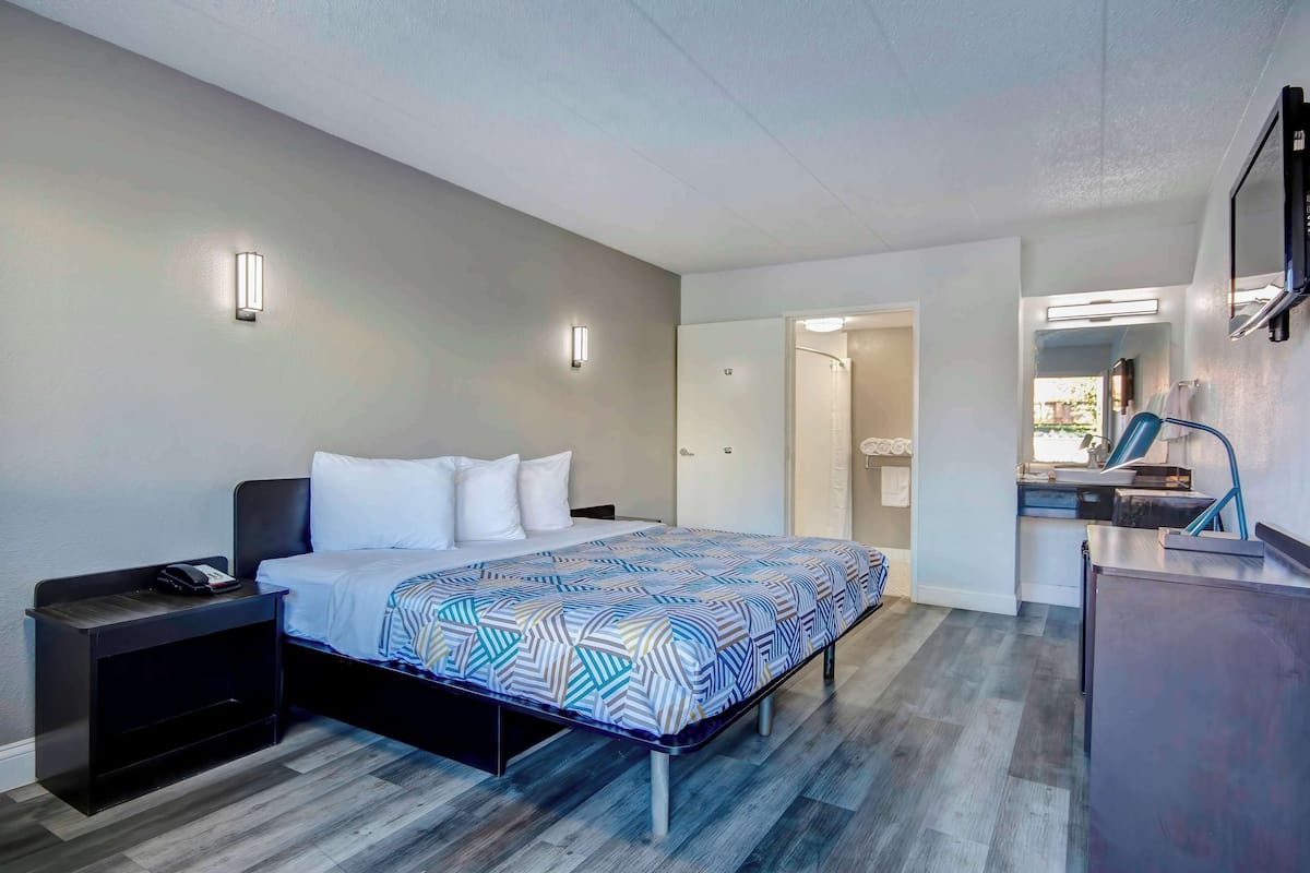 A modern hotel room with a bed, bedside tables, a desk, and a mirror.