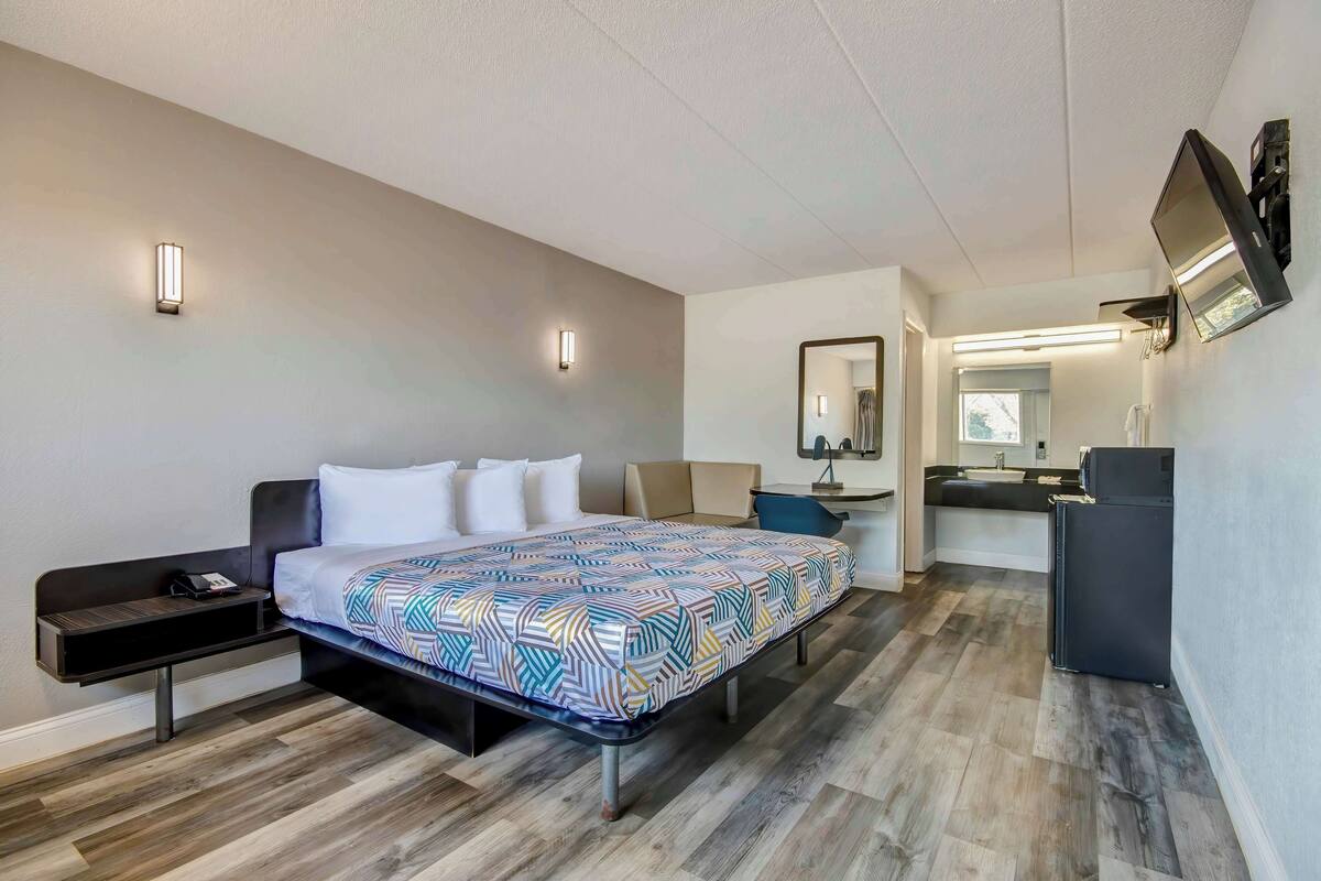 A modern hotel room with a bed, bedside table, and a small desk with a chair.