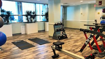 A gym with wooden flooring, exercise equipment, and large windows.