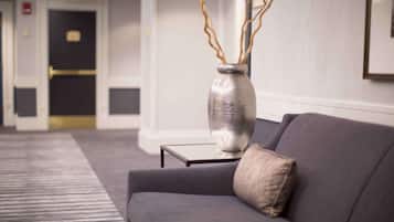 A modern hotel lobby with a grey sofa, a metallic vase with branches, and a framed picture on the wall.