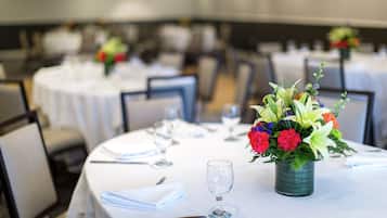 A dining area with round tables set for a meal, each with a vase of flowers, white tablecloths, and neatly arranged cutlery.