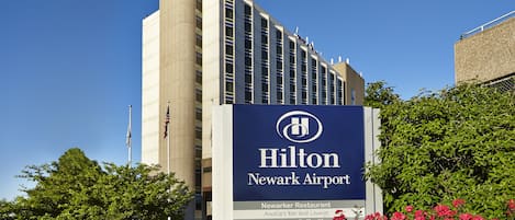 Un edificio del Hilton Newark Airport con un cartel que indica servicios como el restaurante Newarker, el bar y salón Amelia’s y la cafetería Edison’s Brew.