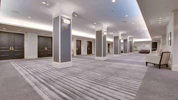 Een ruime hotel lobby met vloerbedekking, meerdere deuren en een zithoek met een tafel en stoelen.