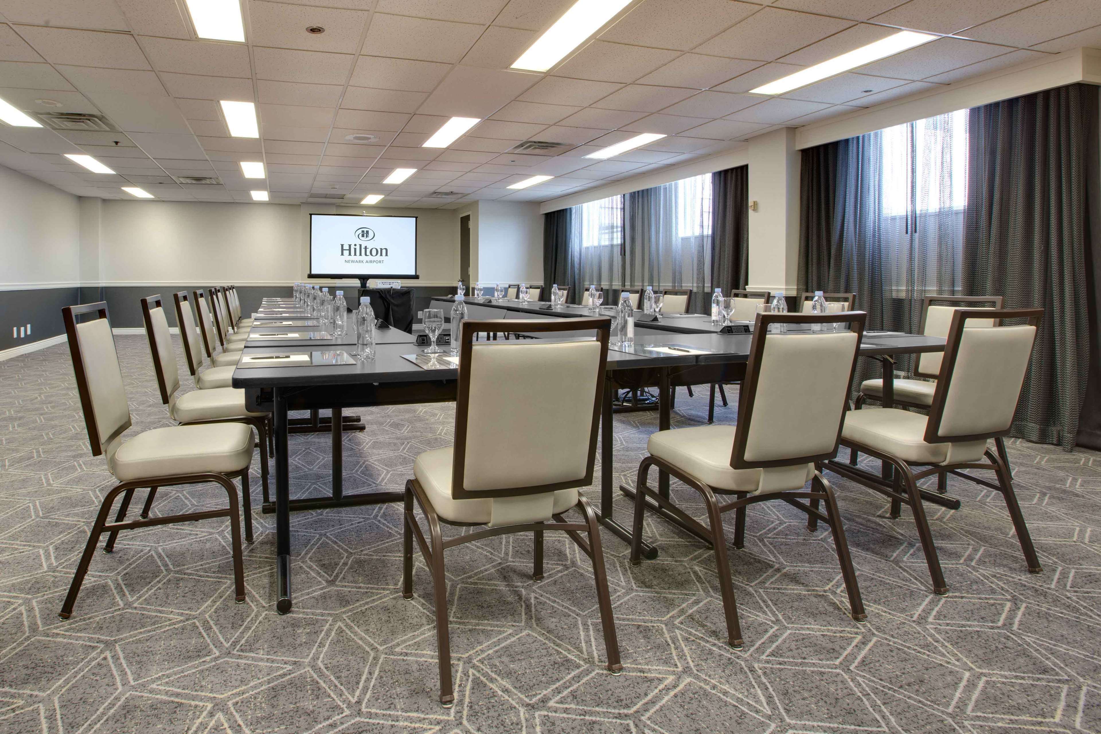 A conference room with a long table, chairs, and a projector screen displaying the Hilton logo.