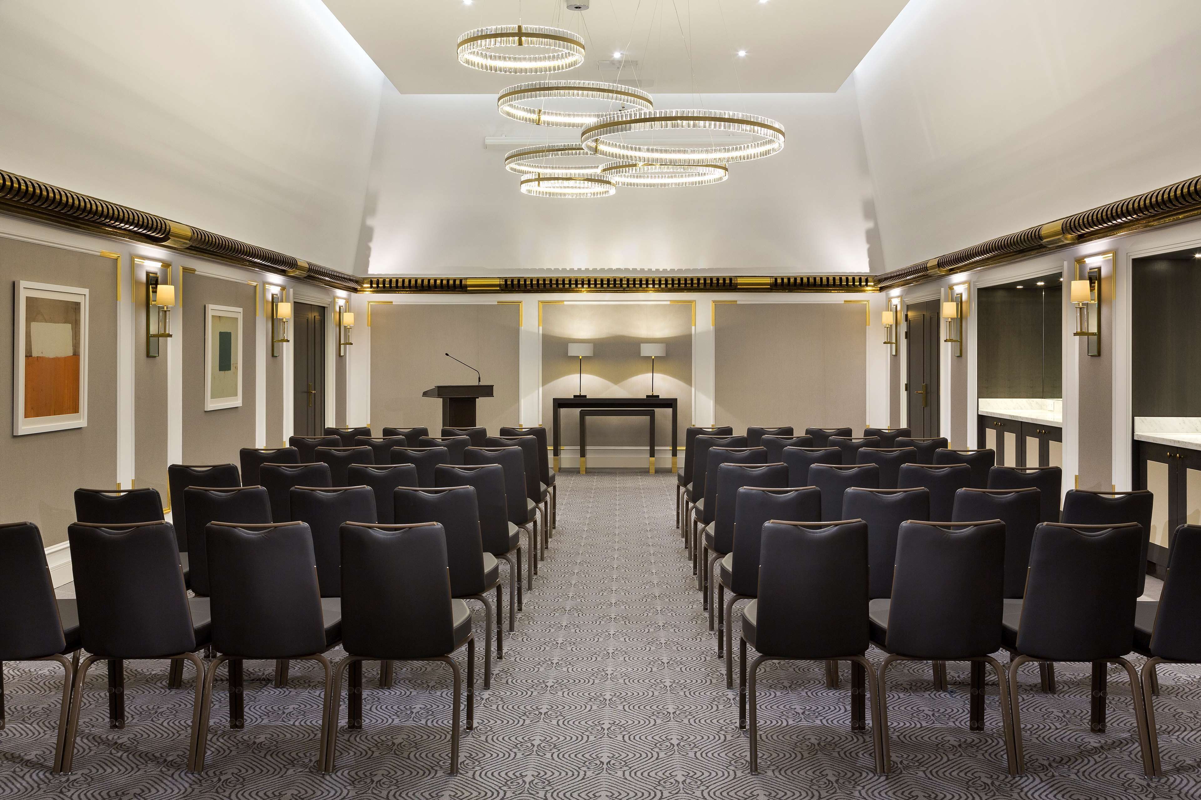 A conference room with rows of chairs, a podium, and wall-mounted lights.