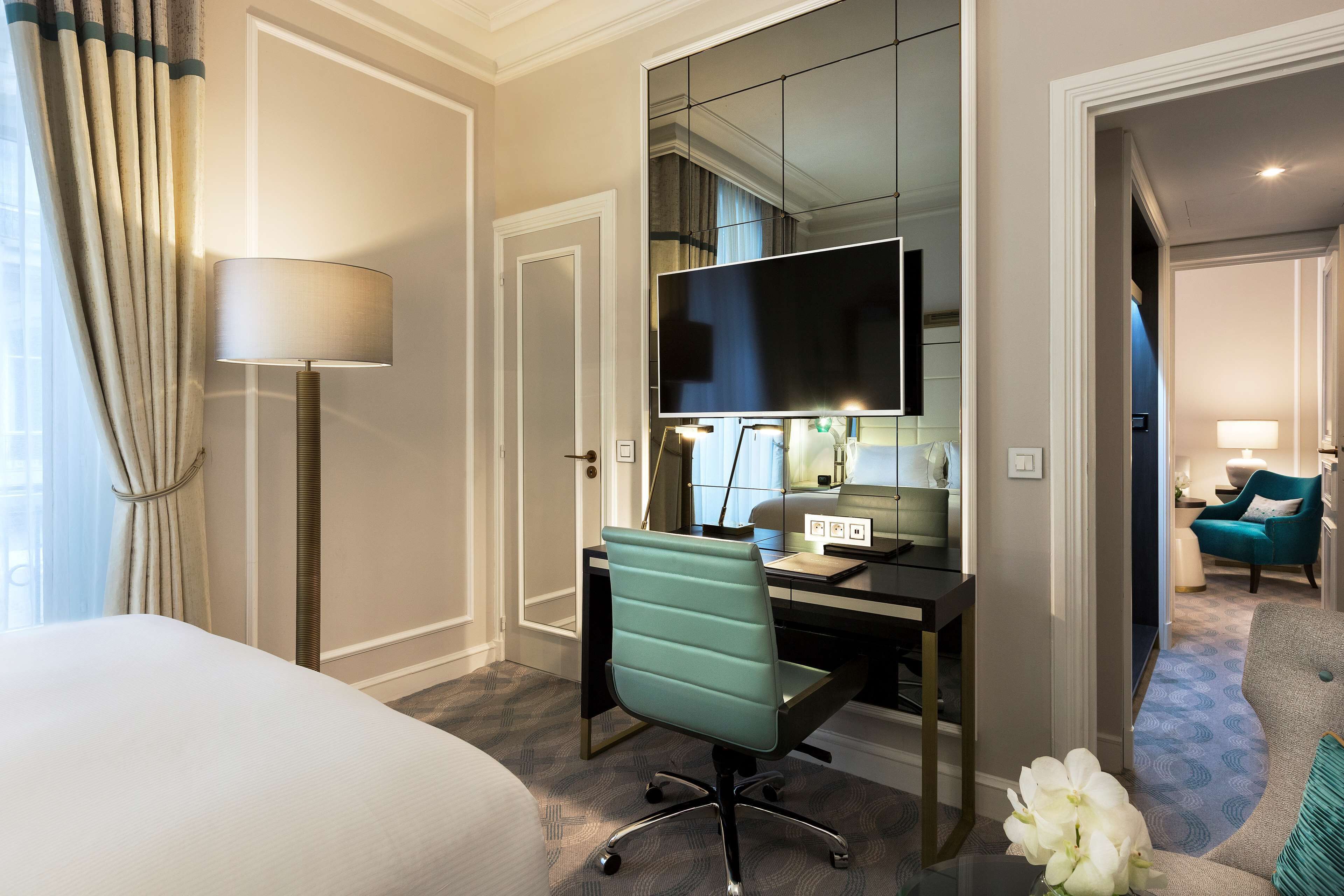 Een hotelkamer met een bed, bureau, stoel, televisie en zicht op een andere kamer.