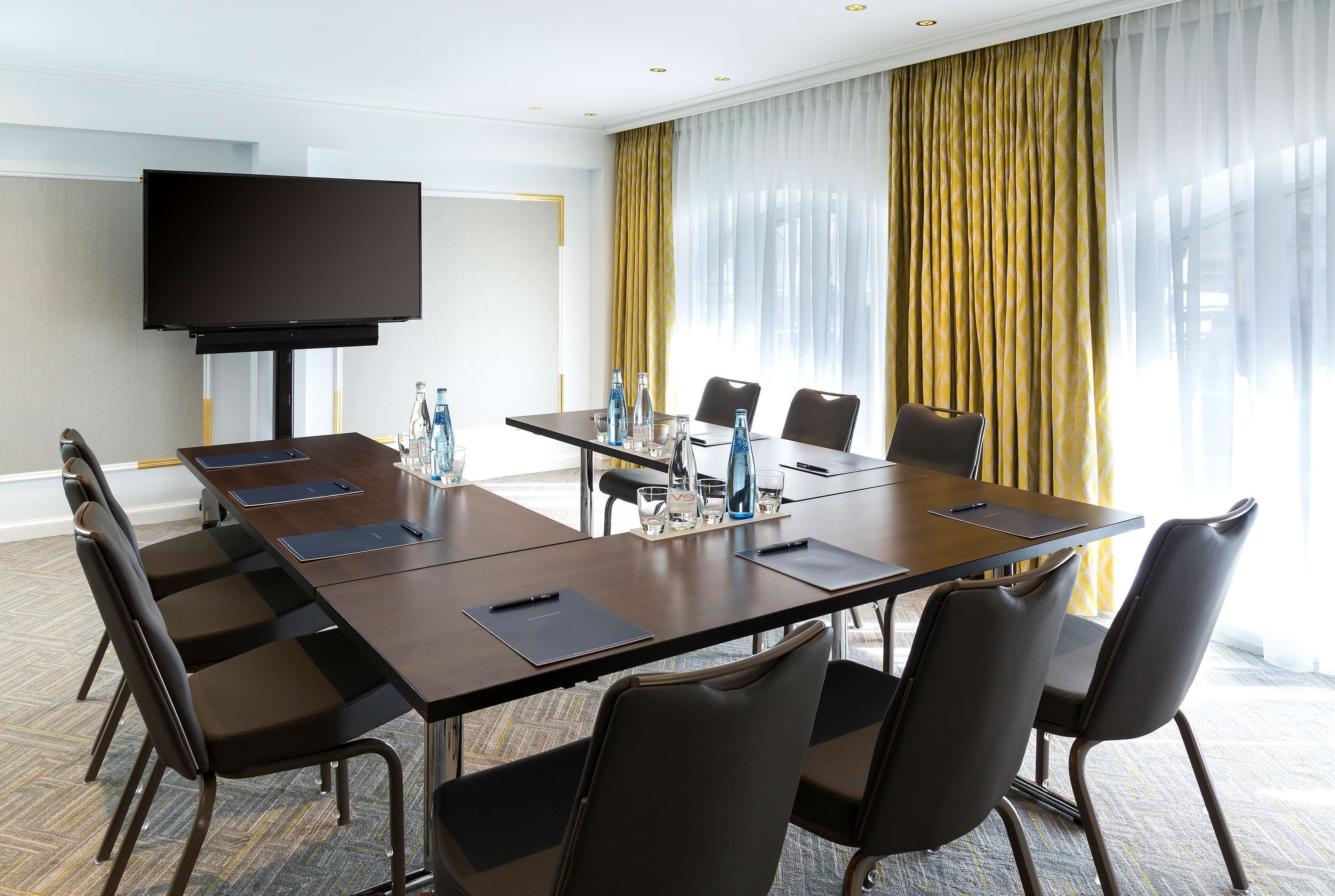 Une salle de conférence équipée d’une grande table, de chaises, d’un téléviseur à écran plat et d’une fenêtre avec des rideaux.