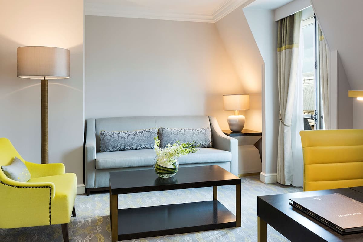 Una habitación de hotel moderna con sofá, dos sillones, una mesa de centro y una lámpara.