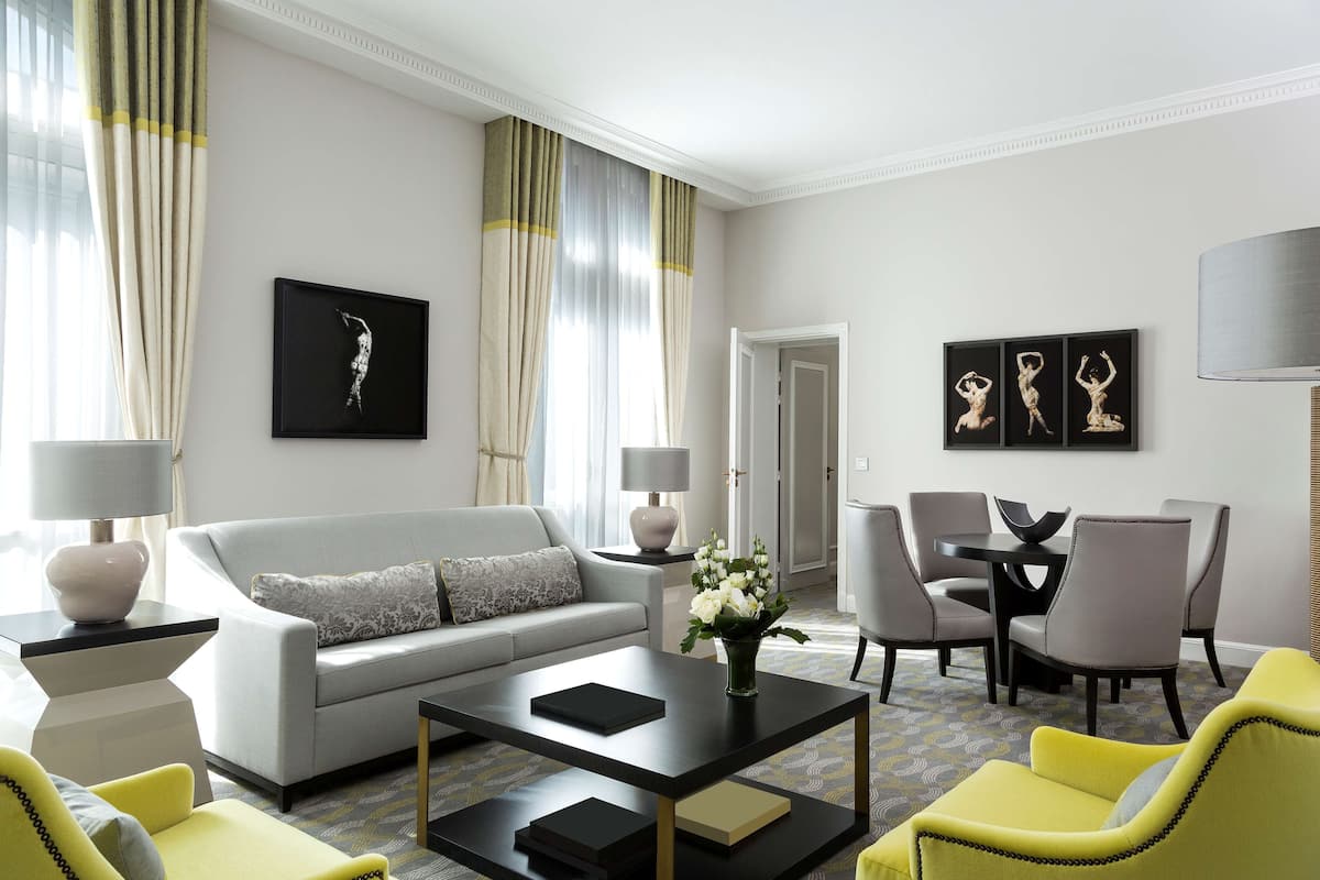 Una sala de estar moderna con un sofá, una mesa de centro y sillones. Se observa una mesa de comedor con sillas y una lámpara.
