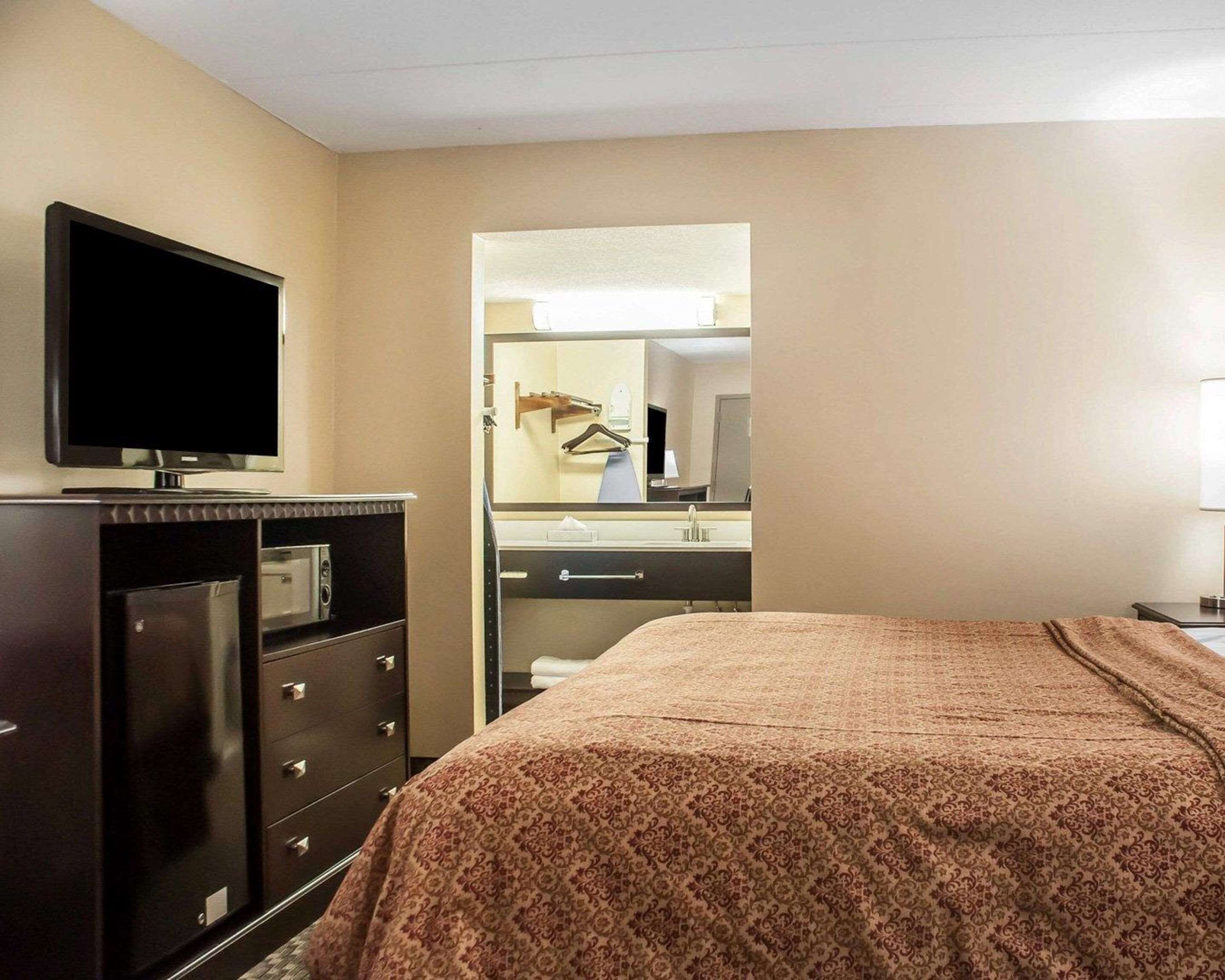 Een hotelkamer met een bed, een televisie op een dressoir, een spiegel en een badkamer die door een open deur zichtbaar is.