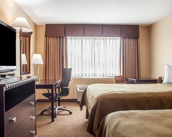 A hotel room with a bed, a desk with a chair, a television, and a window with curtains.