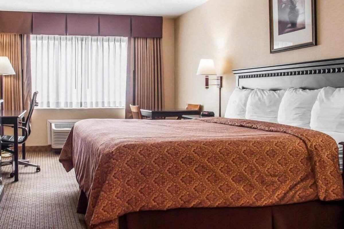 Ein Hotelzimmer mit Bett, Schreibtisch, Stuhl und einem Fenster mit Vorhängen.