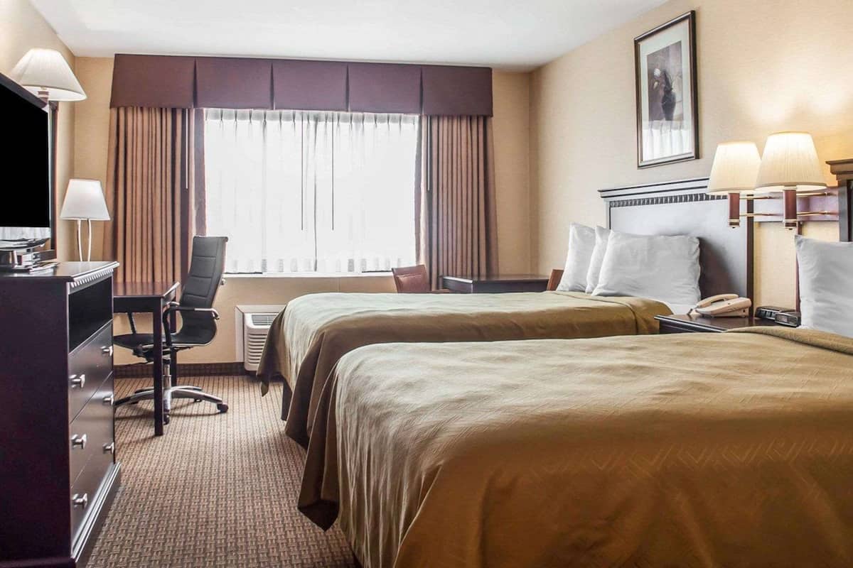 Een hotelkamer met twee bedden, een bureau, een stoel, een televisie en een raam met gordijnen.