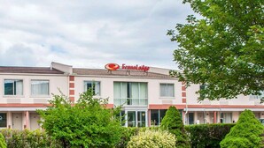 A hotel with a sign reading "Econo Lodge." It features a modern design with a flat roof and large windows. The surrounding area includes well-maintained landscaping with various shrubs and trees.