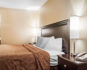 A hotel room with a large bed, a bedside table with a lamp, and a phone.