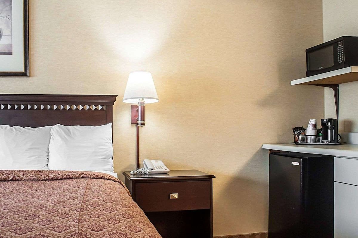 Een hotelkamer met een bed, een bedlampje, een telefoon, een koffiezetapparaat en een magnetron.