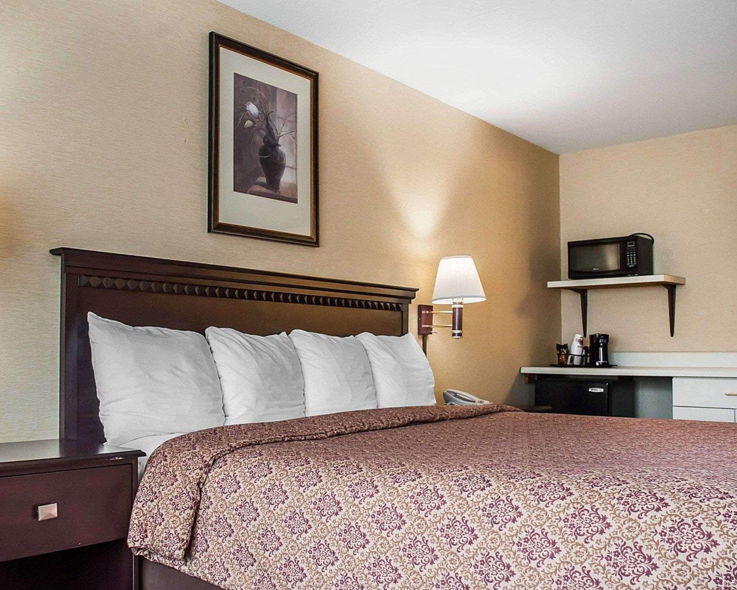 Una habitación de hotel con cama, mesita de noche, lámpara, microondas y cafetera.