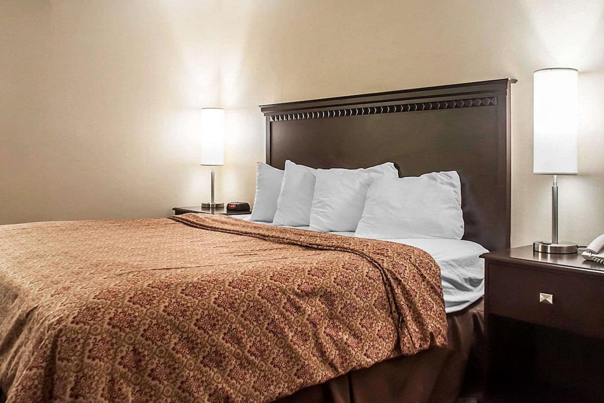 Een hotelkamer met een groot bed, een nachtkastje met een lamp en een aan de muur bevestigde telefoon.