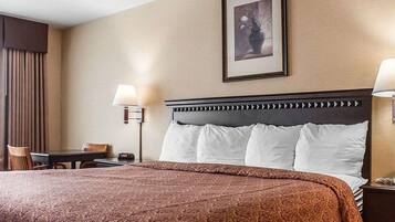 A hotel room with a large bed, two bedside lamps, a framed picture on the wall, and a small table with a chair.