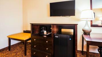 Habitación de hotel con un escritorio de madera, una silla amarilla, un minibar, un televisor y una lámpara.