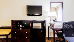 A hotel room with a dark wooden desk, a flat-screen TV mounted above it, a small table with a lamp, and a black office chair. - Quality Inn Dillon (Dillon)