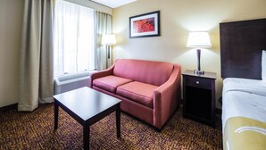 A hotel room with a bed, a sofa, a table, two lamps, a window with curtains, and a framed picture on the wall. - Quality Inn Dillon (Dillon)