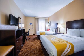 A hotel room with two beds, a desk, a chair, a TV, and a window with curtains.