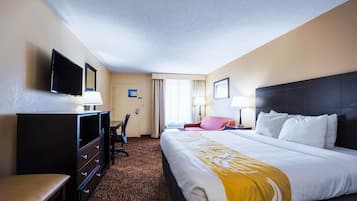 A hotel room with a large bed, a desk, a chair, a television, and a window with curtains.