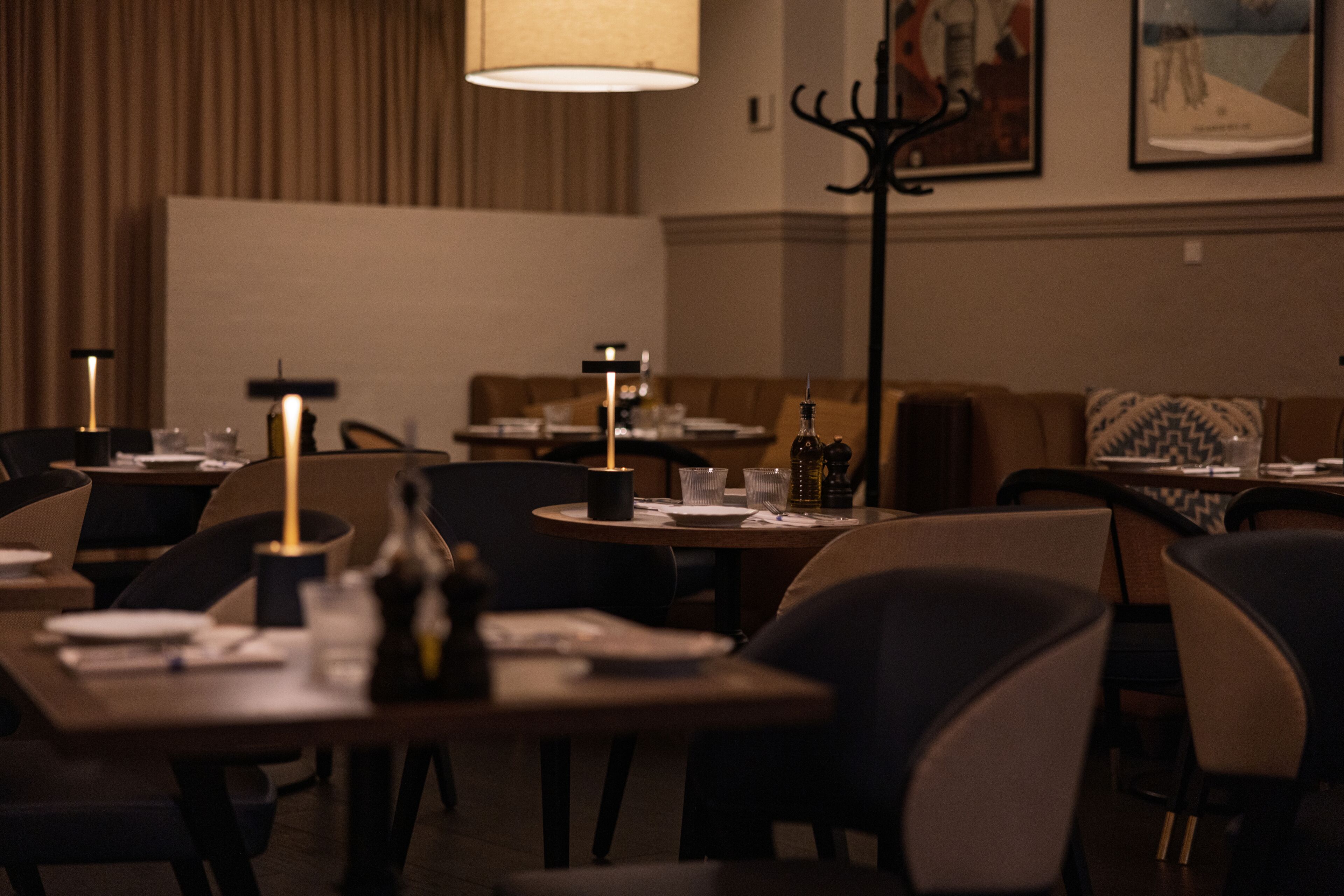 A dimly lit restaurant with tables set for dining, featuring a warm ambiance and modern decor.