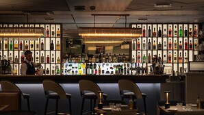 A bar area with a bartender, shelves of liquor bottles, and bar stools. - Phoenix Copenhagen (Copenhagen)